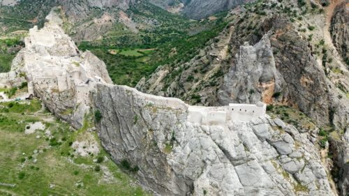 Video - Aerial drone view of a historic fortress built along dramatic mountain cliffs overlooking a canyon valley, highlighting ancient architecture and landscapes of the Mesopotamia region
