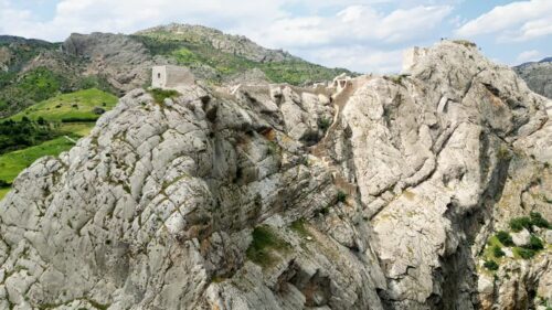 Video - Aerial drone view of a historic fortress built along dramatic mountain cliffs overlooking a canyon valley, highlighting ancient architecture and landscapes of the Mesopotamia region