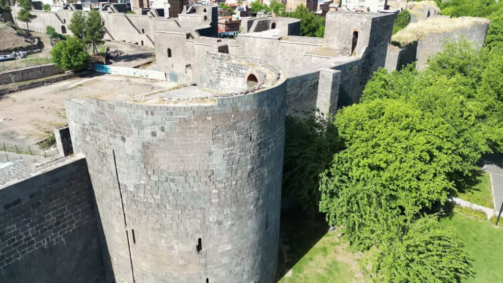 Video - Aerial drone view of ancient stone fortress walls and towers rising above a town, showcasing historic architecture in Mesopotamia