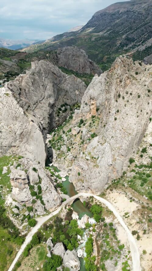 Video - Aerial drone view of a narrow river flowing between steep rocky canyon walls, highlighting dramatic natural formations in the Mesopotamia region. Vertical