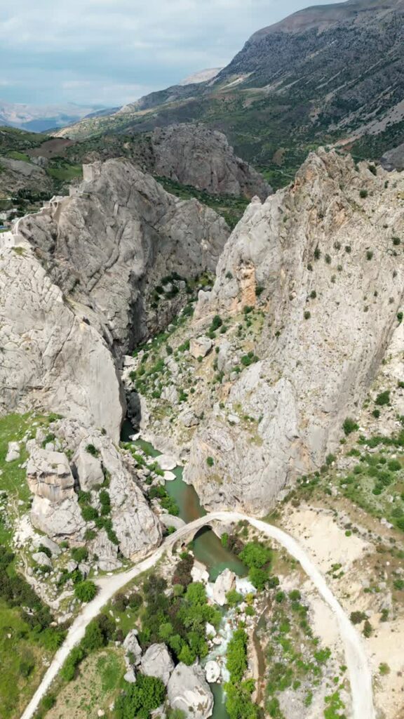 Video - Aerial drone view of a narrow river flowing between steep rocky canyon walls, highlighting dramatic natural formations in the Mesopotamia region. Vertical