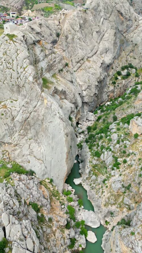 Video - Aerial drone view of a narrow river flowing between steep rocky canyon walls, highlighting dramatic natural formations in the Mesopotamia region. Vertical
