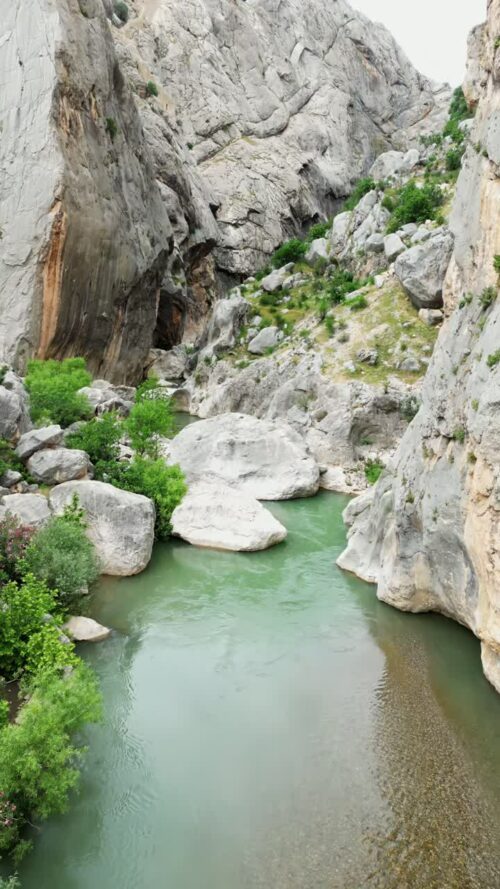 Video - Aerial drone view of a mountain river flowing under a small bridge surrounded by rocks and green trees in a canyon valley in Mesopotamia. Vertical
