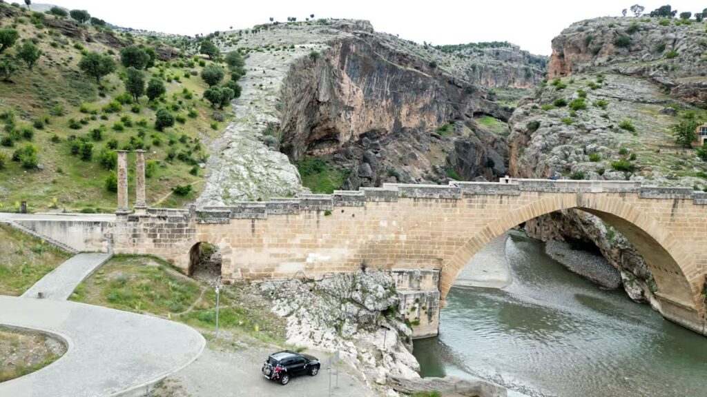 Video - Aerial drone view of Malabadi Bridge, a historic stone arch bridge crossing the Batman River in southeastern Turkey, surrounded by rocky canyon landscapes in the Mesopotamia region