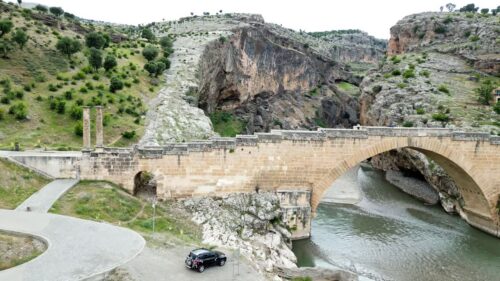 Video - Aerial drone view of Malabadi Bridge, a historic stone arch bridge crossing the Batman River in southeastern Turkey, surrounded by rocky canyon landscapes in the Mesopotamia region