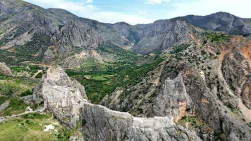 Video - Aerial drone view of a historic fortress built along dramatic mountain cliffs overlooking a canyon valley, highlighting ancient architecture and landscapes of the Mesopotamia region
