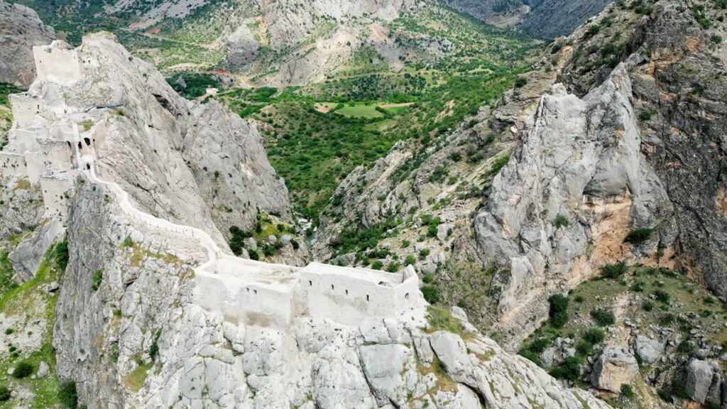 Video - Aerial drone view of a historic fortress built along dramatic mountain cliffs overlooking a canyon valley, highlighting ancient architecture and landscapes of the Mesopotamia region