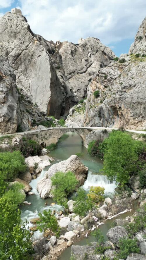 Video - Aerial drone view of Malabadi Bridge, a historic stone arch bridge crossing the Batman River in southeastern Turkey, surrounded by rocky canyon landscapes in the Mesopotamia region. Vertical
