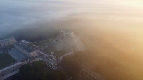 Video - Aerial drone view of the Temple of the Inscriptions at Palenque archaeological site emerging through morning mist in the Chiapas jungle, Mexico, showing ancient Mayan ruins surrounded by dense rainforest
