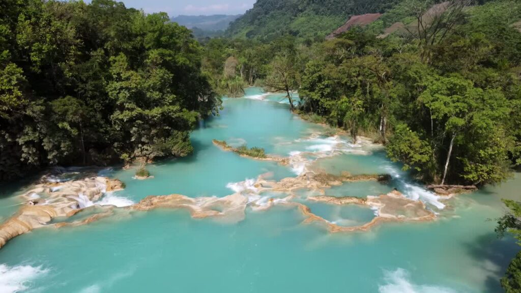 Video - Aerial drone view multiple turquoise waterfalls and natural pools surrounded by dense tropical forest at Agua Azul in southern Mexico