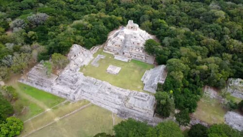 Video - Aerial drone view revealing a historic Mayan temple complex surrounded by lush jungle vegetation in Mexico