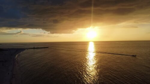 Video - Aerial drone view of a dramatic golden sunset over the ocean along the Mexican coastline. A small boat crosses the calm sea leaving a long wake beneath colorful clouds and warm evening light