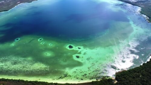 Video - Aerial drone view of shallow turquoise Caribbean waters with coral reef formations and sandbanks along tropical coastline