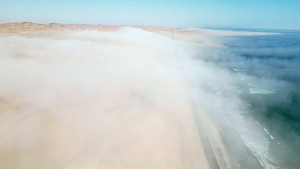 Video - Aerial drone view of coastal fog moving over vast desert dunes along the Atlantic Ocean in Namibia creating a dramatic atmospheric landscape