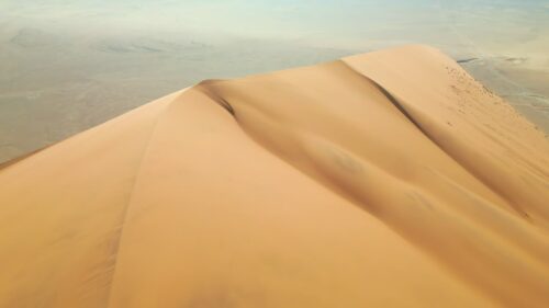 Video - Aerial drone view along the ridge of a towering sand dune in the Namib Desert highlighting the wind-shaped patterns and textures of the sand