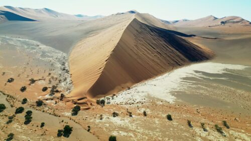 Video - Aerial drone view of a massive triangular sand dune rising above the desert plains in Namibia with sparse desert vegetation