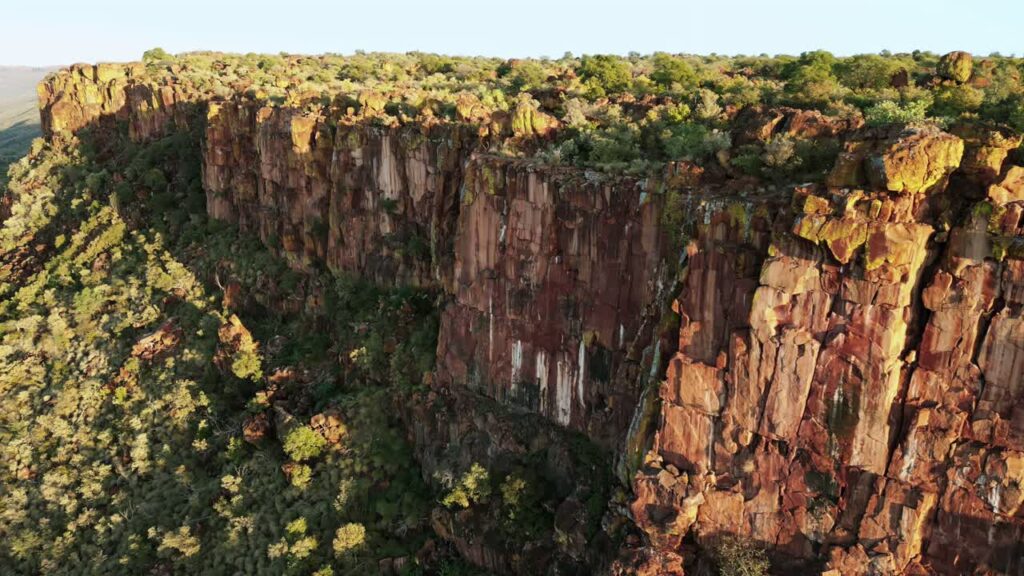 Video - Aerial drone view of dramatic rocky cliffs rising above a green savanna landscape in Namibia during warm golden hour light