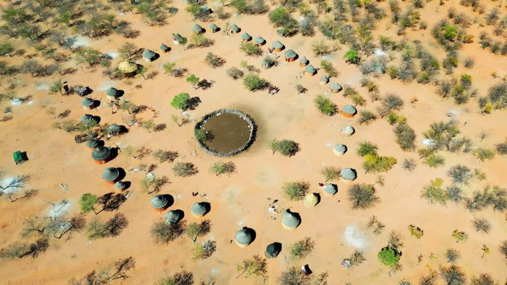 Video - Aerial drone view of a traditional circular Himba village settlement in northern Namibia with huts arranged around a central livestock enclosure