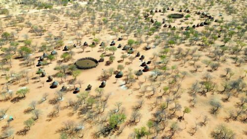 Video - Aerial drone view of a traditional circular Himba village settlement in northern Namibia with huts arranged around a central livestock enclosure