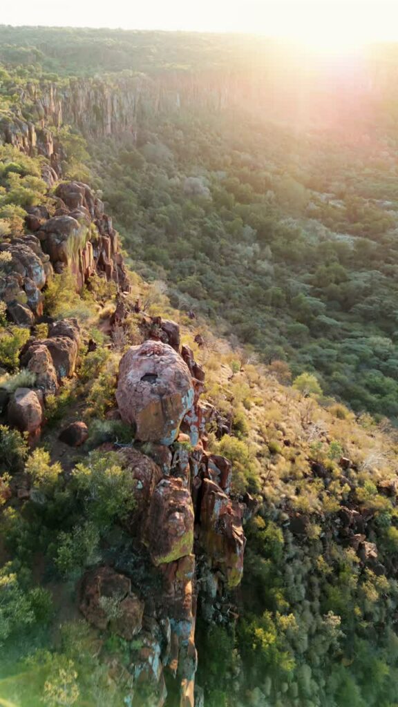 Video - Aerial drone view of dramatic rocky cliffs and green vegetation in Namibia during warm sunset light overlooking a vast wilderness valley. Vertical