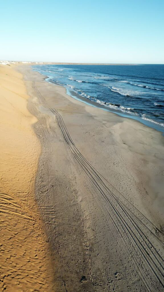 Video - Aerial drone view of the remote Skeleton Coast shoreline in Namibia showing waves breaking along a vast sandy beach and desert dunes. Vertical