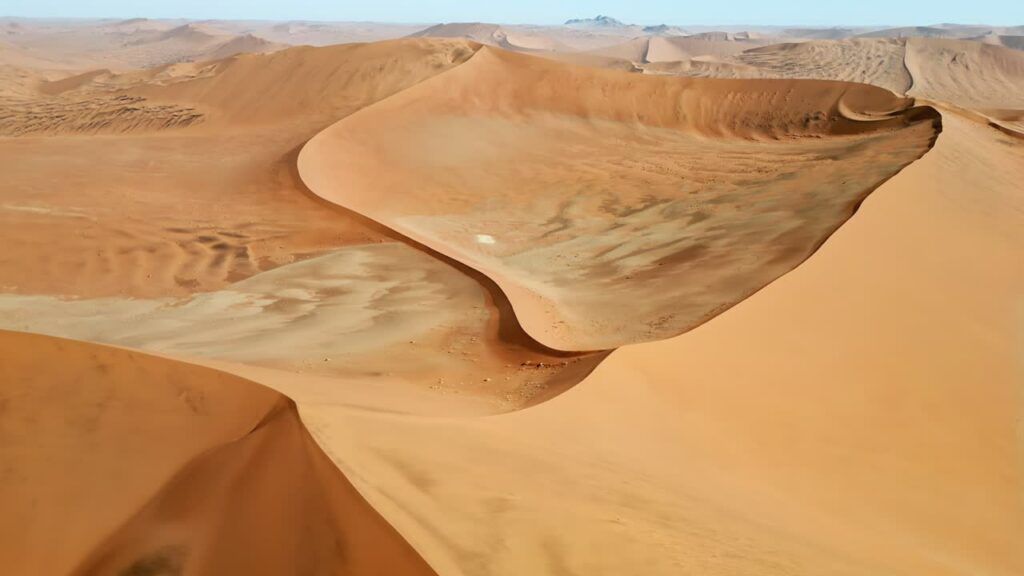 Video - Aerial drone view of sweeping sand dune formations in the Namib Desert showing elegant curves and wind shaped patterns across the landscape