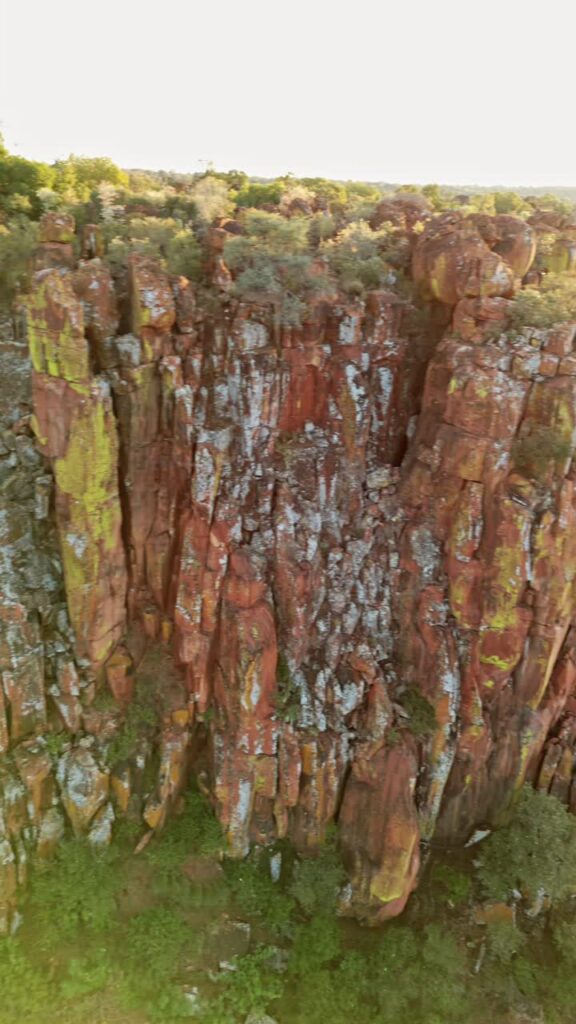 Video - Aerial drone view of dramatic rocky cliffs and green vegetation in Namibia during warm sunset light overlooking a vast wilderness valley. Vertical