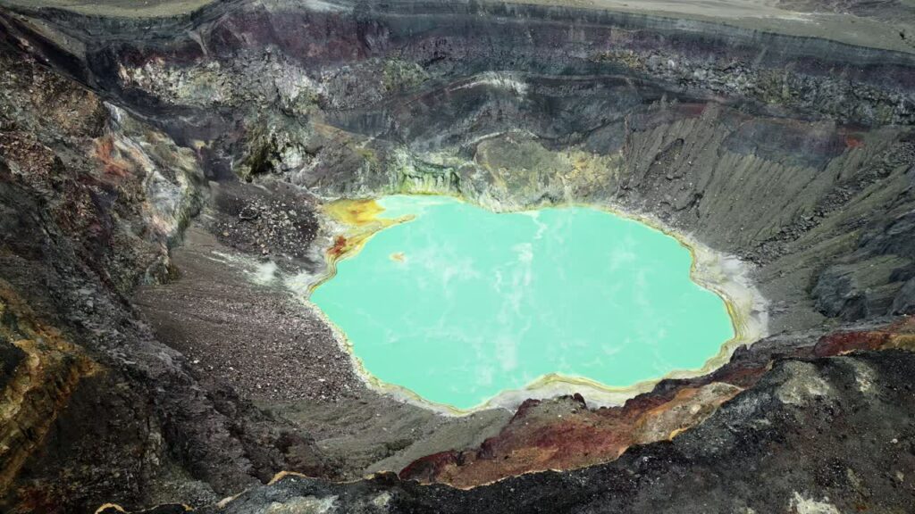 Video - Aerial drone view of a turquoise crater lake inside a volcanic crater in Guatemala, surrounded by rugged volcanic rock formations and geothermal landscape