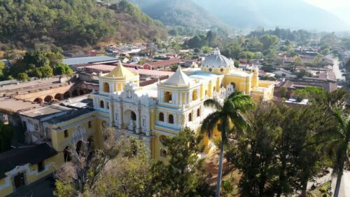 Video - Aerial drone view of the iconic yellow La Merced Church in Antigua Guatemala surrounded by colonial buildings and palm trees