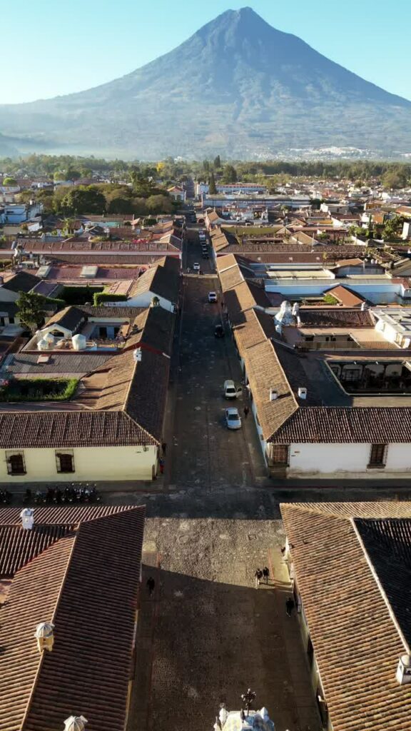 Video - Aerial drone view of a colonial street in Antigua Guatemala aligned with Volcan de Agua rising in the distance. Vertical