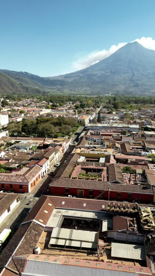 Video - Aerial drone view of a colonial street in Antigua Guatemala aligned with Volcan de Agua rising in the distance. Vertical