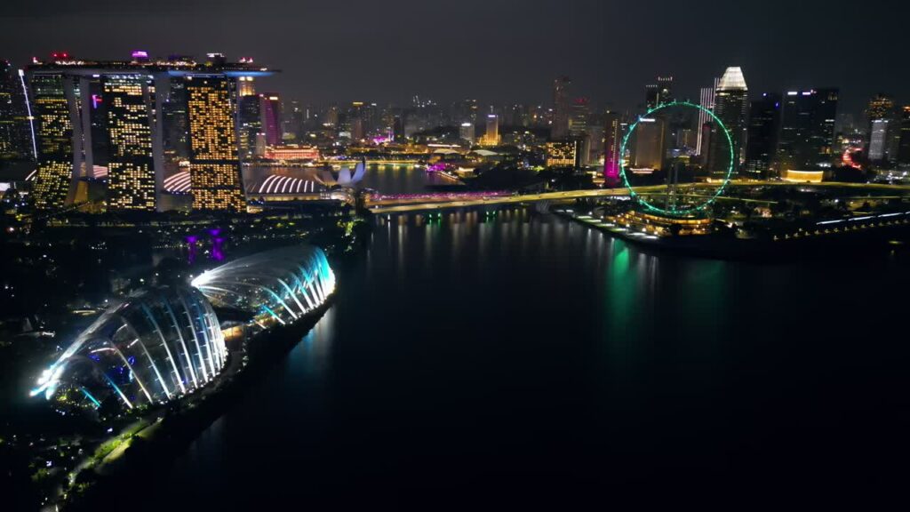 Video - Aerial drone view of Marina Bay in Singapore at night showing Marina Bay Sands, the Singapore Flyer observation wheel, and illuminated waterfront skyline