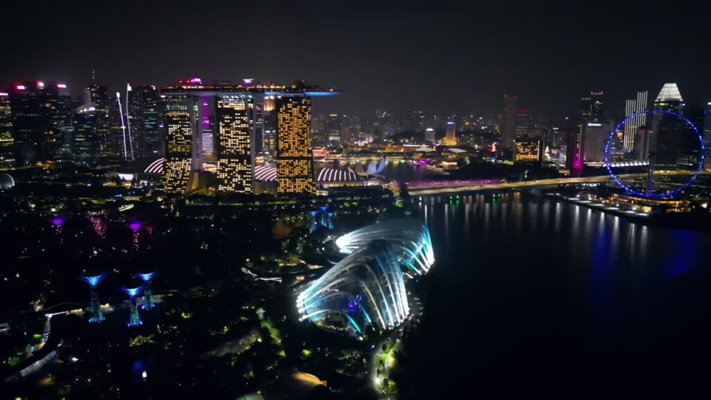 Video - Aerial drone view of Marina Bay in Singapore at night showing Marina Bay Sands, the Singapore Flyer observation wheel, and illuminated waterfront skyline