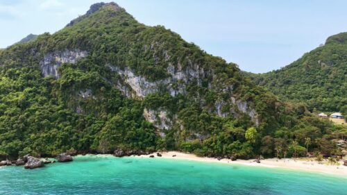 Video - Aerial drone view of a tropical beach in Thailand surrounded by limestone cliffs and turquoise water along the Andaman Sea coastline