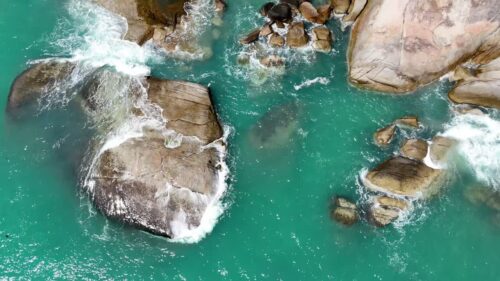 Video - Aerial drone view of ocean waves breaking against large coastal rocks in turquoise water in Thailand