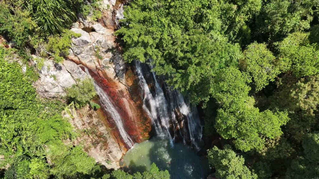 Video - Aerial drone view of a tropical waterfall flowing through dense jungle vegetation in Thailand