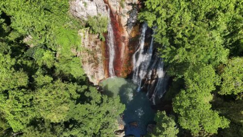 Video - Aerial drone view of a tropical waterfall flowing through dense jungle vegetation in Thailand