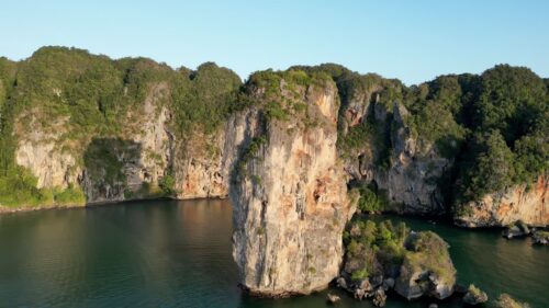 Video - Aerial drone view of a limestone sea stack rising from calm tropical waters in southern Thailand