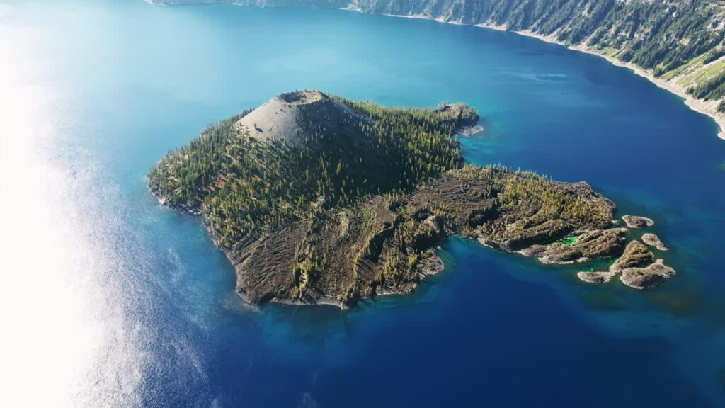 Video - Aerial drone view of Wizard Island volcano cone rising from the deep blue waters of Crater Lake National Park, Oregon