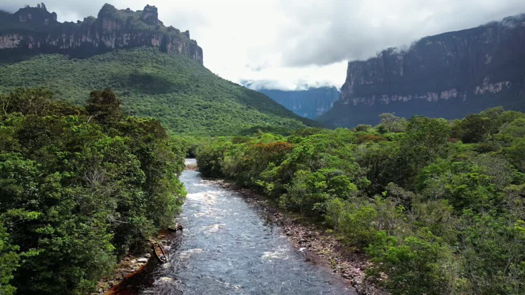 Video - Aerial drone view of a tropical river flowing through dense rainforest surrounded by the dramatic tepui mountains in Canaima National Park, Venezuela