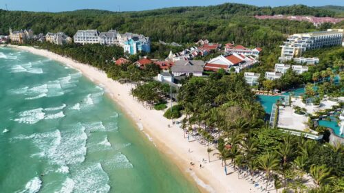 Video - Aerial drone view of a tropical beach resort with palm trees and turquoise ocean waves along the coastline in Vietnam